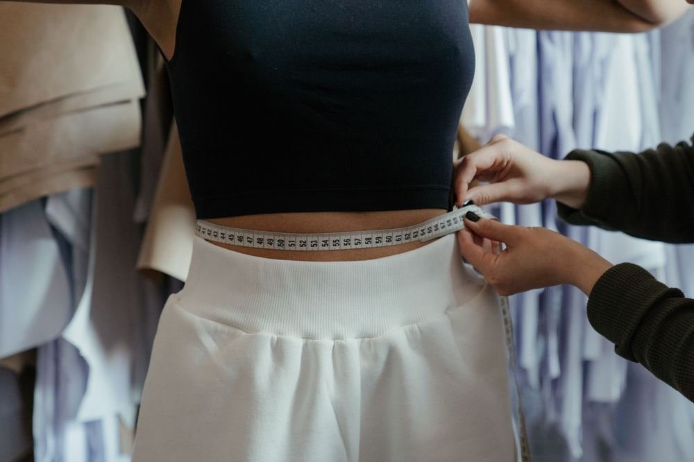 Tailor measuring a woman's natural waist with a soft tape measure for a body shape calculator