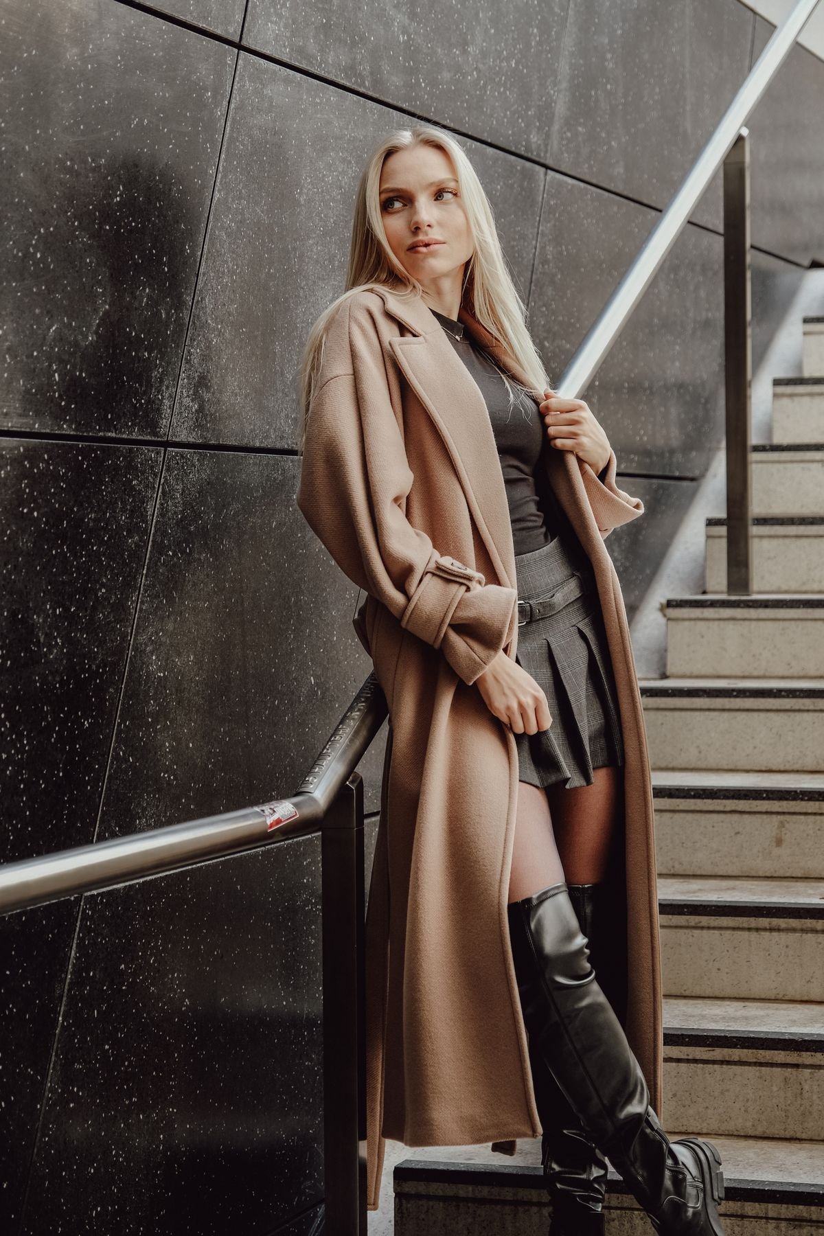 Woman wearing a camel coat over a midi dress with knee-high boots