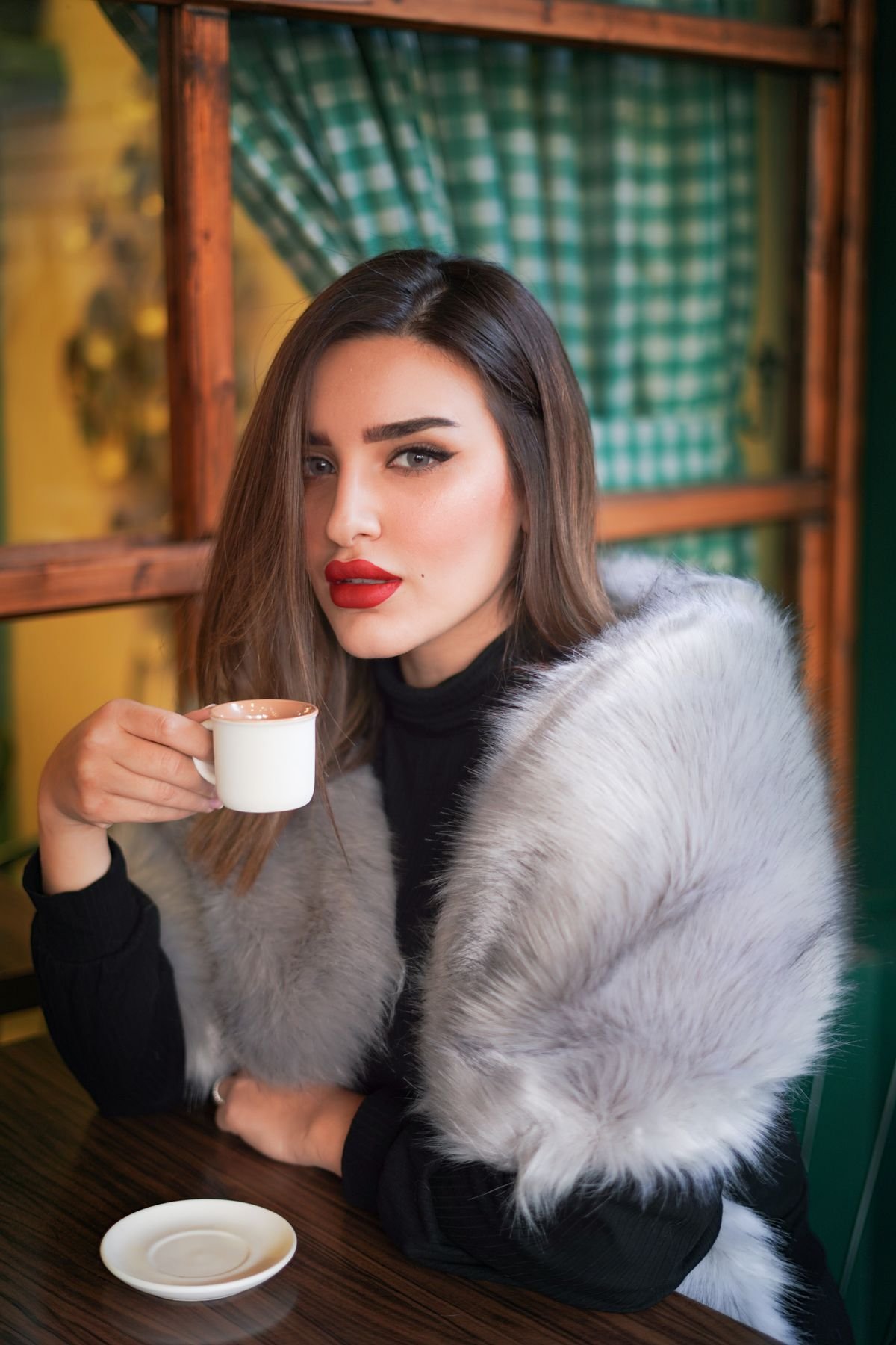 Woman wearing a grey fur scarf while drinking coffee indoors