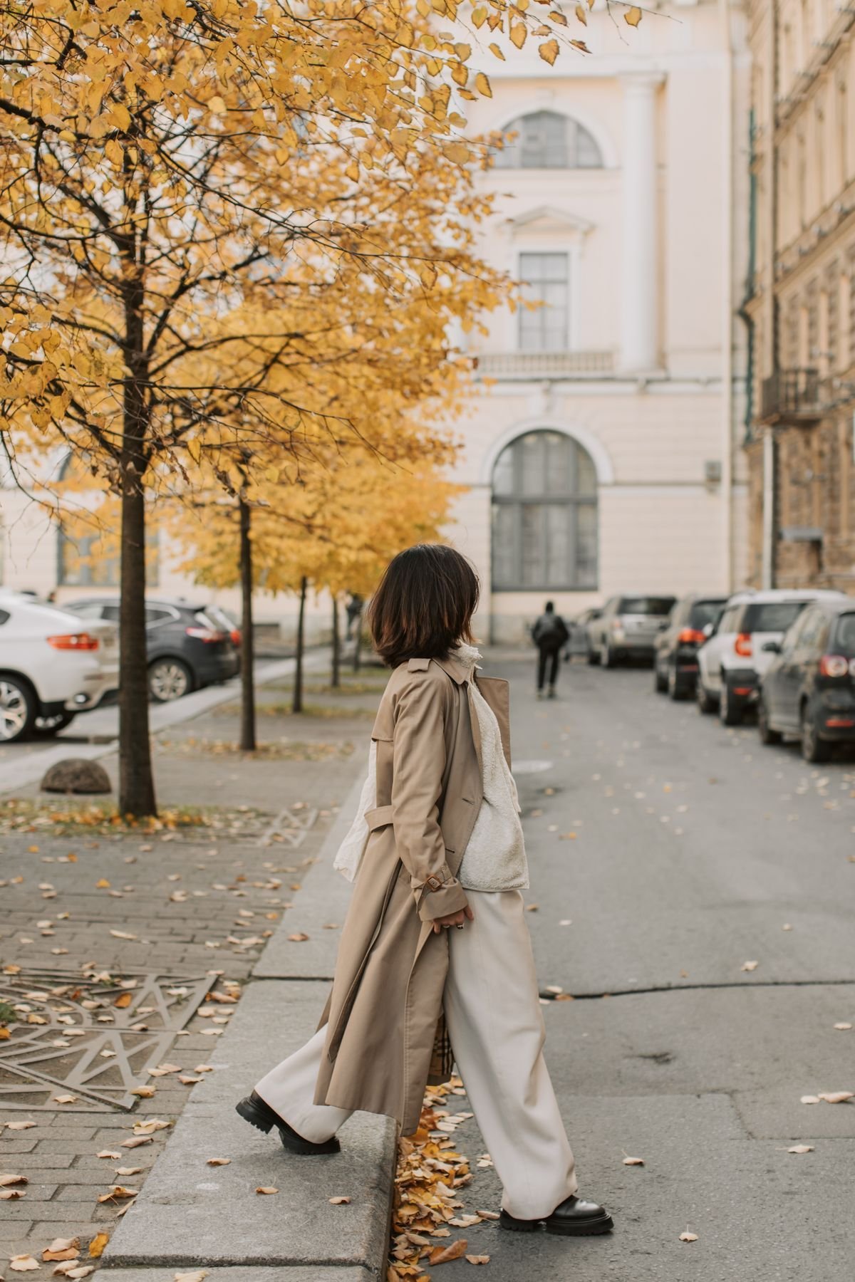 Woman layering a cream fleece gilet under a trench coat on an autumn street