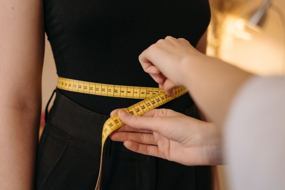 Tailor measuring a woman's waist with a yellow tape for accurate clothing size conversion