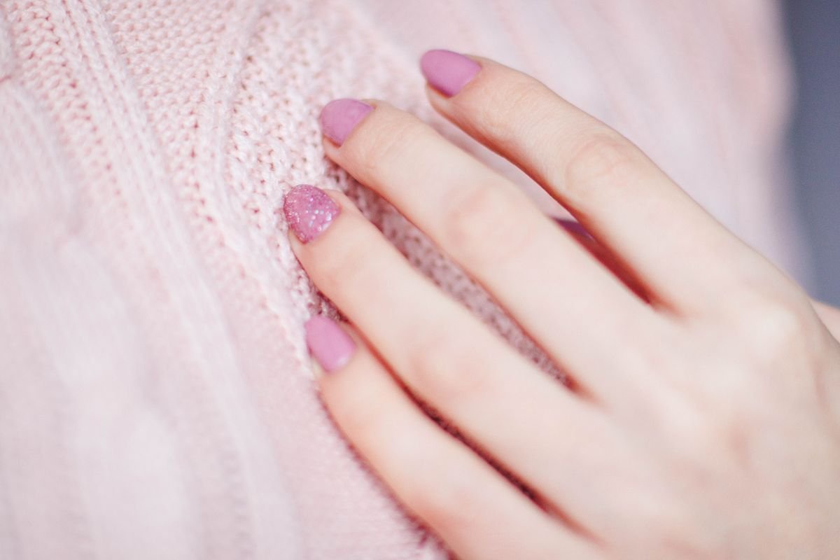 Close-up of a hand with a pink manicure resting on a soft knit sweater